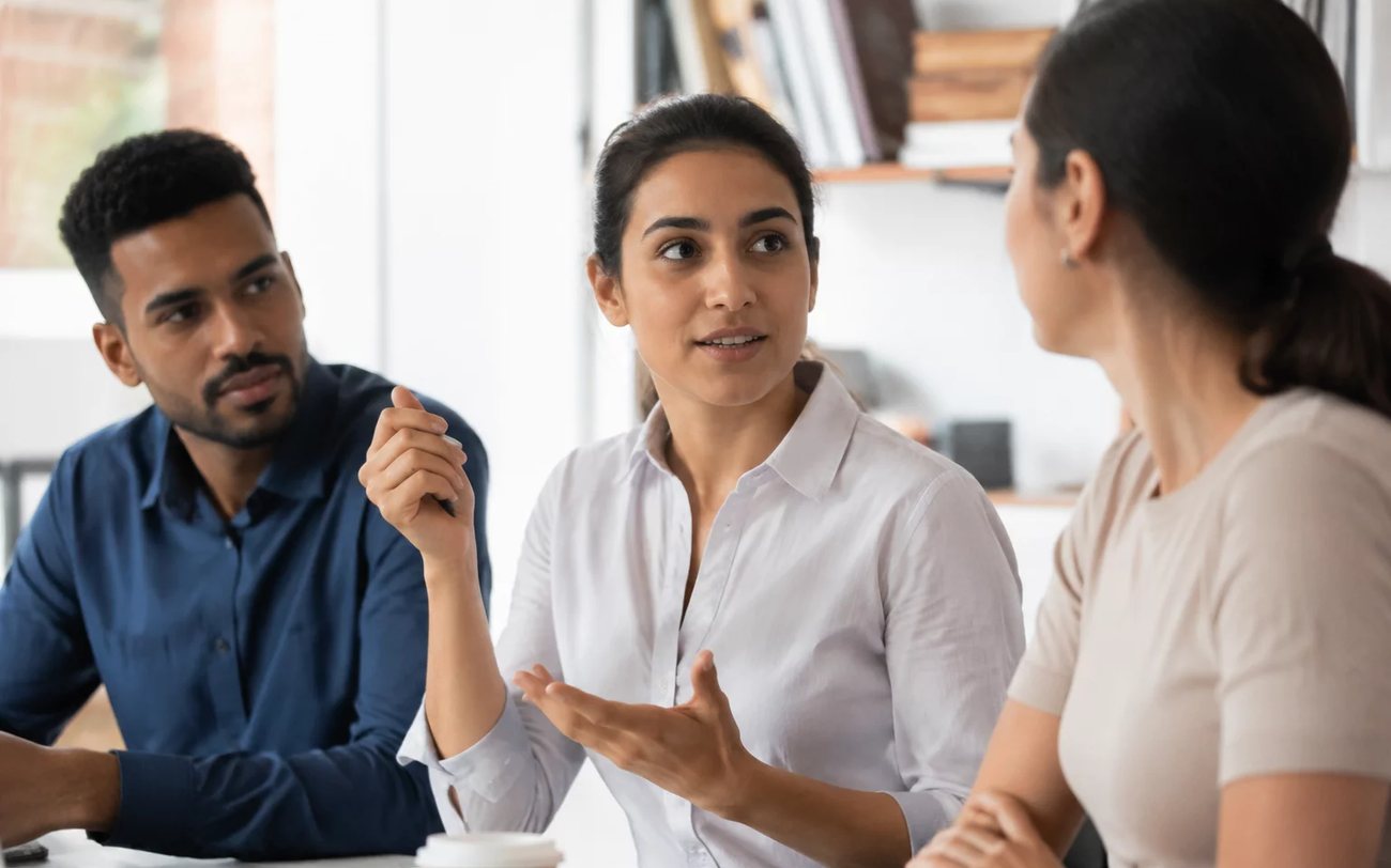 Roda de conversa numa sala clara, com uma pessoa expondo o ponto e duas escutando